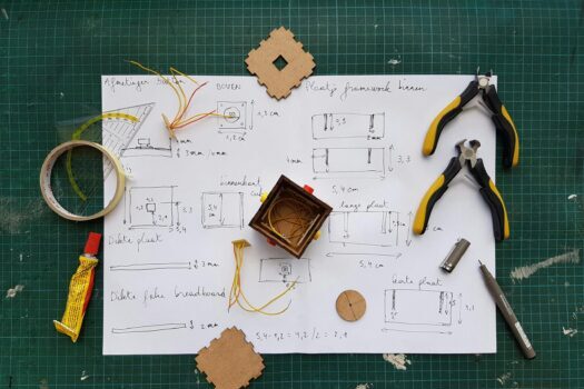 Overhead view of DIY electronics project with components and tools on grid mat.